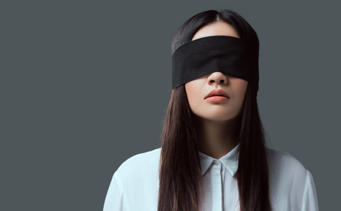 young woman wearing black blindfold isolated on grey