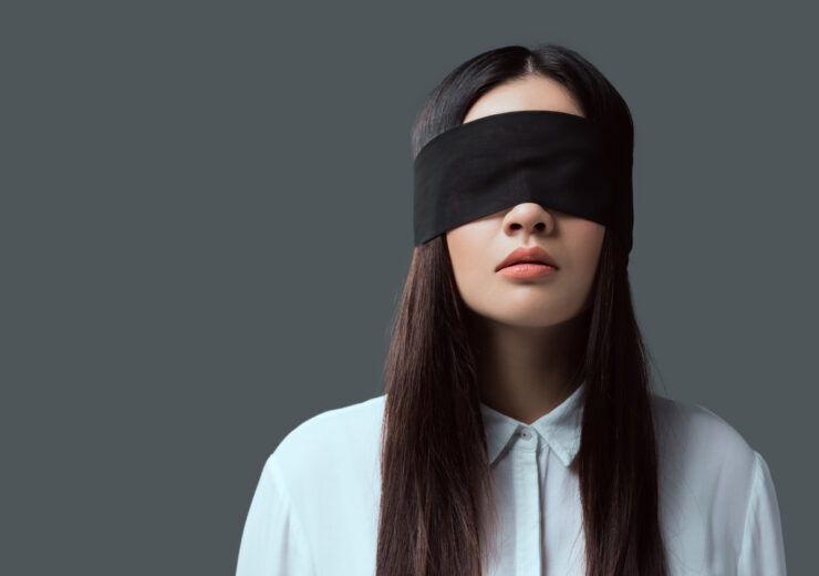 young woman wearing black blindfold isolated on grey