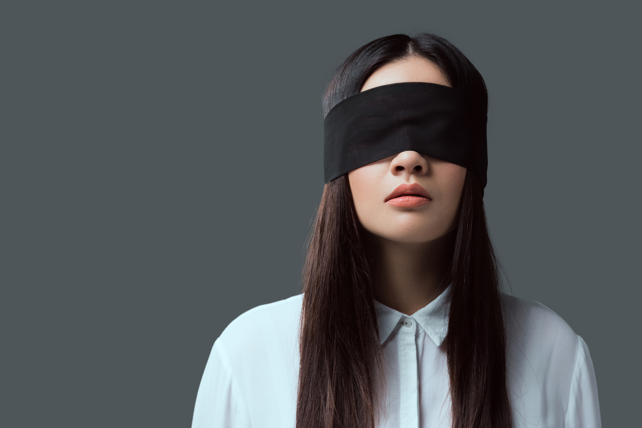 young woman wearing black blindfold isolated on grey