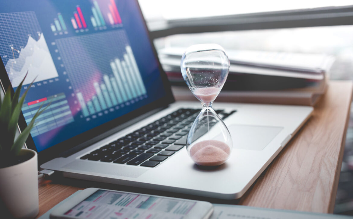 Business concepts with businessman holding hourglass with graph chart on computer laptop