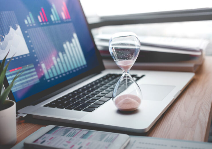 Business concepts with businessman holding hourglass with graph chart on computer laptop