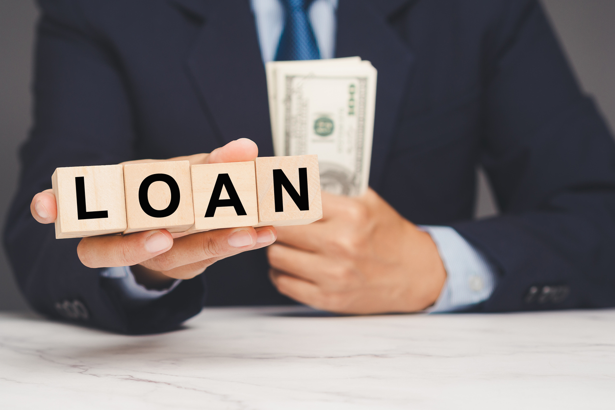 Businessman holding loan blocks and cash, representing financial borrowing and banking concept.