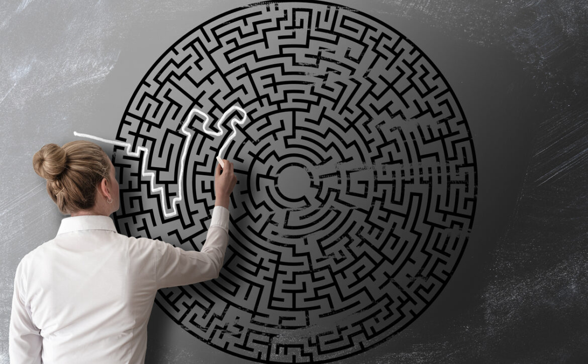 woman trying to find way through chalk drawing of maze on blackboard challenge concept