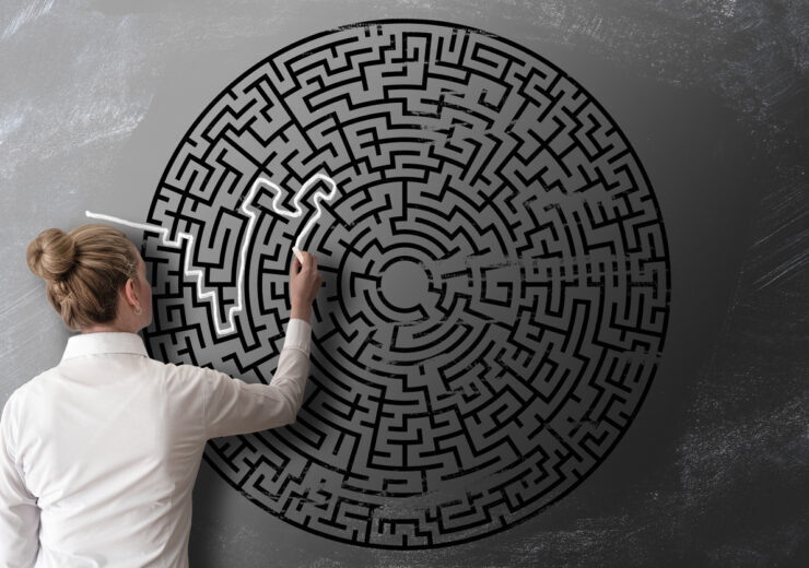 woman trying to find way through chalk drawing of maze on blackboard challenge concept