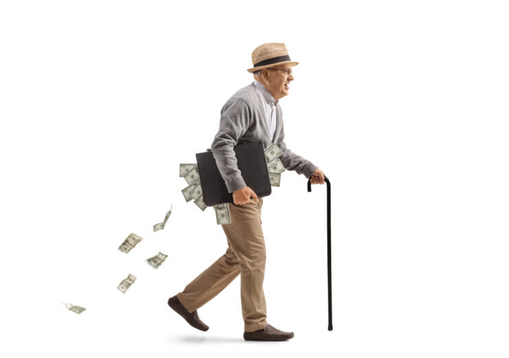 Full length profile shot of an edlery man walking with a cane and carrying a briefcase full of money isolated on white background