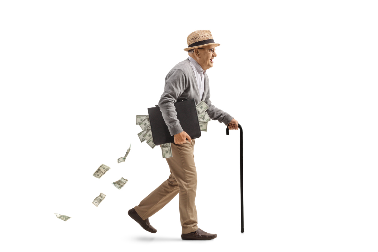 Full length profile shot of an edlery man walking with a cane and carrying a briefcase full of money isolated on white background