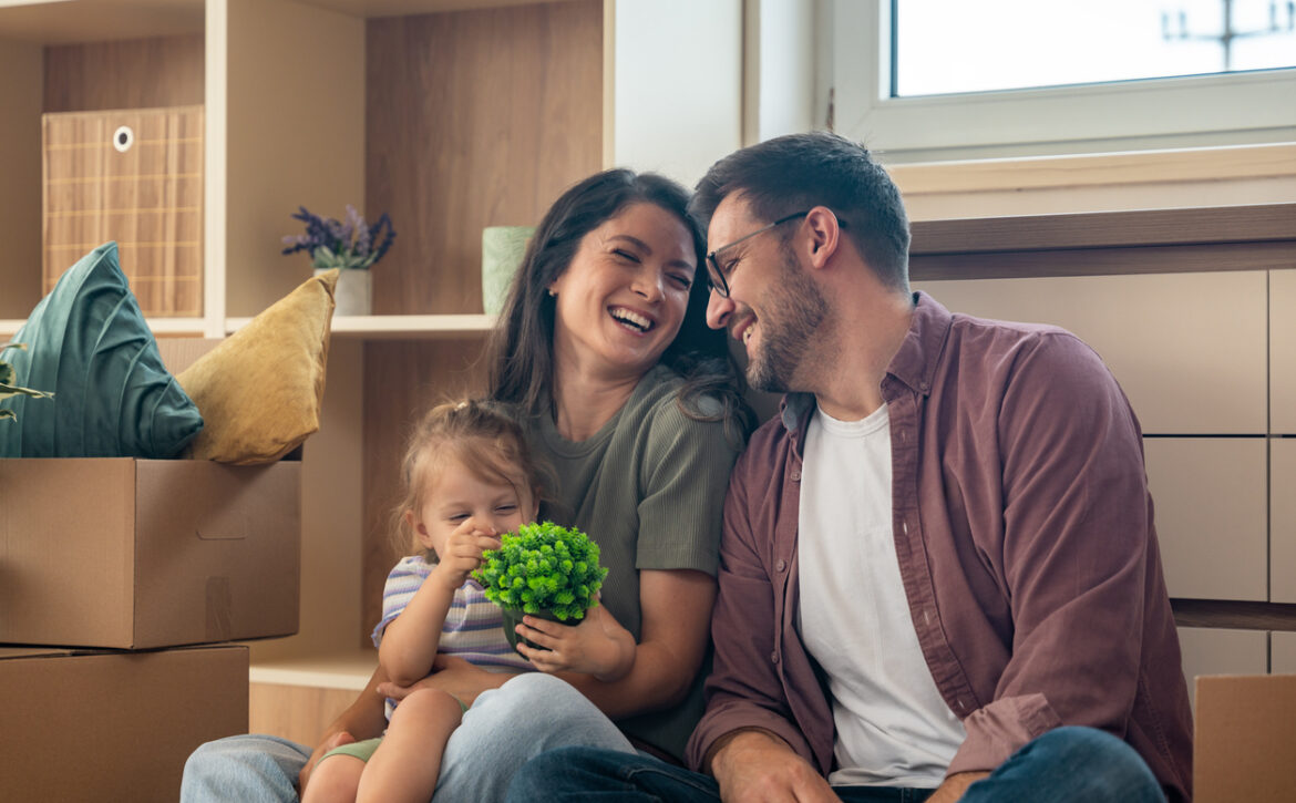 Young couple with their daughter happily moving into their new apartment after buying it with a bank loan. First-time homeowners enjoying freedom after years of renting, smiling in their new home.