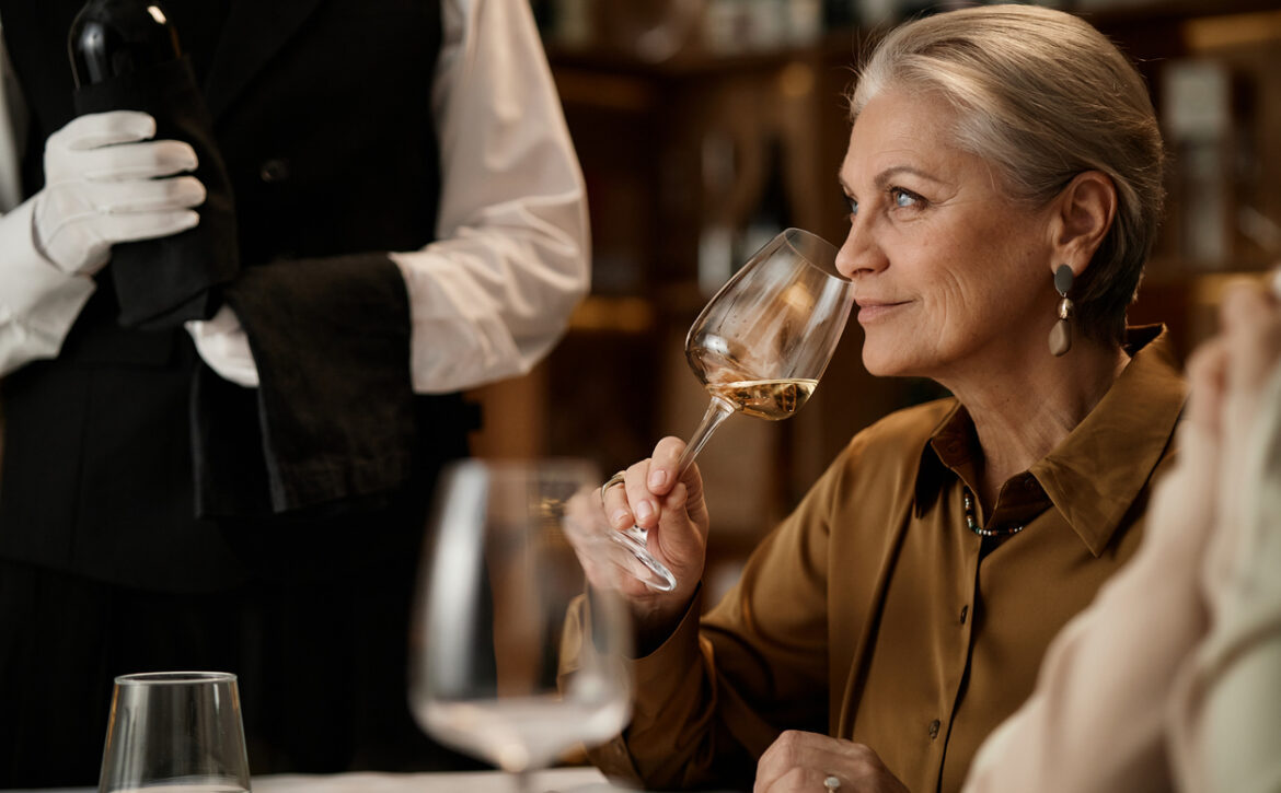 Senior Caucasian Woman Smelling Wine While Sitting at Table in Restaurant