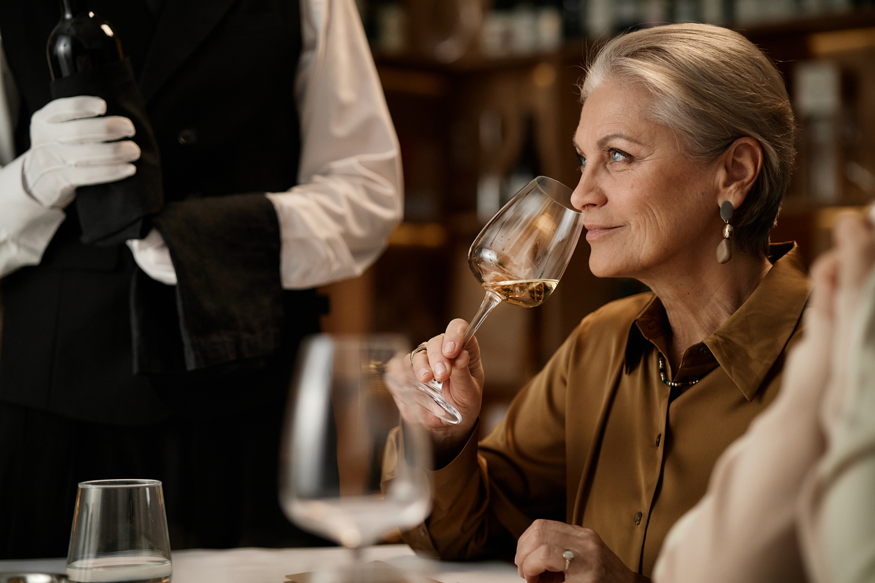 Senior Caucasian Woman Smelling Wine While Sitting at Table in Restaurant