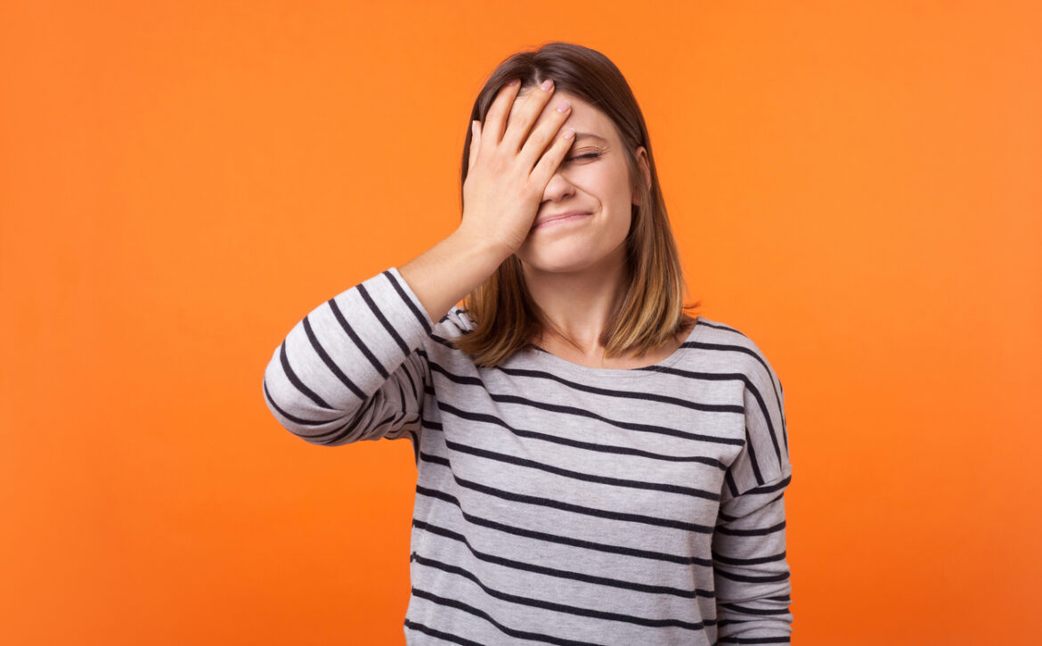 Facepalm. Portrait of forgetful upset woman with brown hair in long sleeve shirt. indoor studio shot isolated on orange background