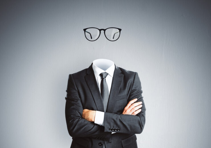 Headless invisible businessman in suit with folded arms and abstract glasses standing on gray wall background. Business and secret concept.
